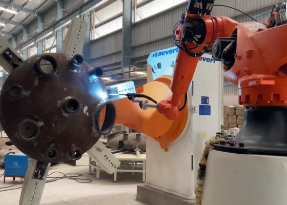 Advantage Plus robotic welding cell: an orange welding robot welding a nozzle on a dished vessel end held on a positioner